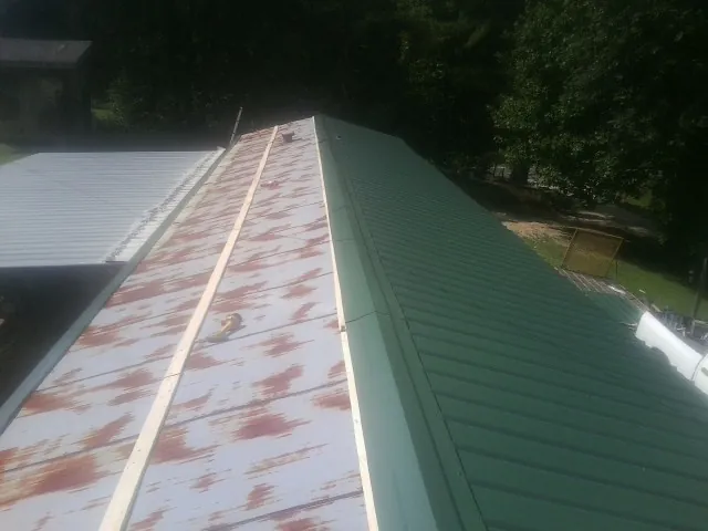 Old rusted panels beside newly installed green metal roofing — Wind Damage Roof Repair by Roofing Brothers in Liberty
