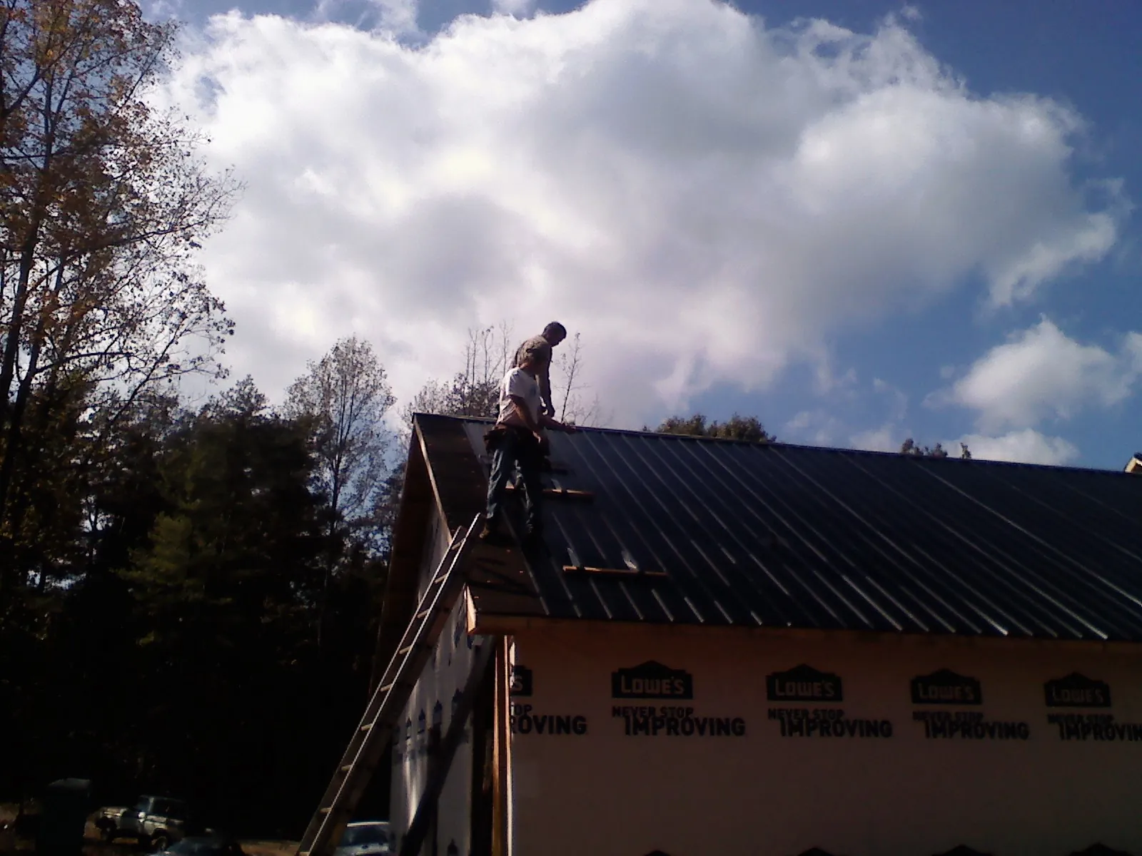 Roofer fastening dark metal panels high against a cloudy sky, from a Roof Inspection job in Liberty
